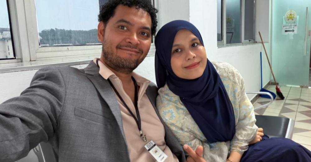 Dr Nor Atiqah Mohamad Alwi bergambar bersama suaminya ketika berada di ruang menunggu mahkamah. Kedua-duanya dilihat duduk bersebelahan sambil tersenyum ke arah kamera.