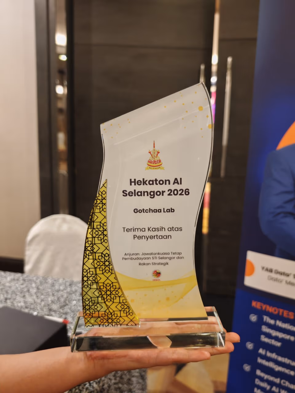 Gotchaa Lab's Hekaton AI Selangor 2026 plaque, held up in front of a keynote banner at the awards event