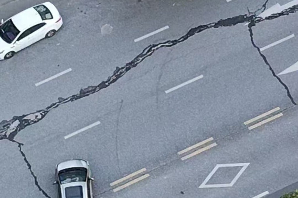 A road with a large crack running through it and two cars parked on it.