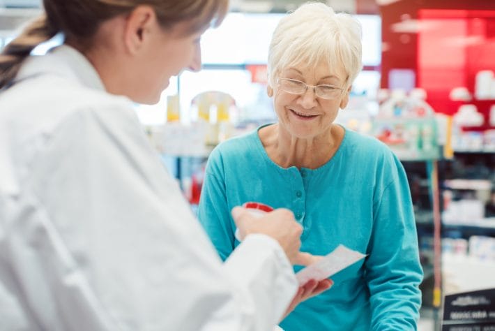 Senior woman discussing prescription medications with a pharmacist at a pharmacy counter