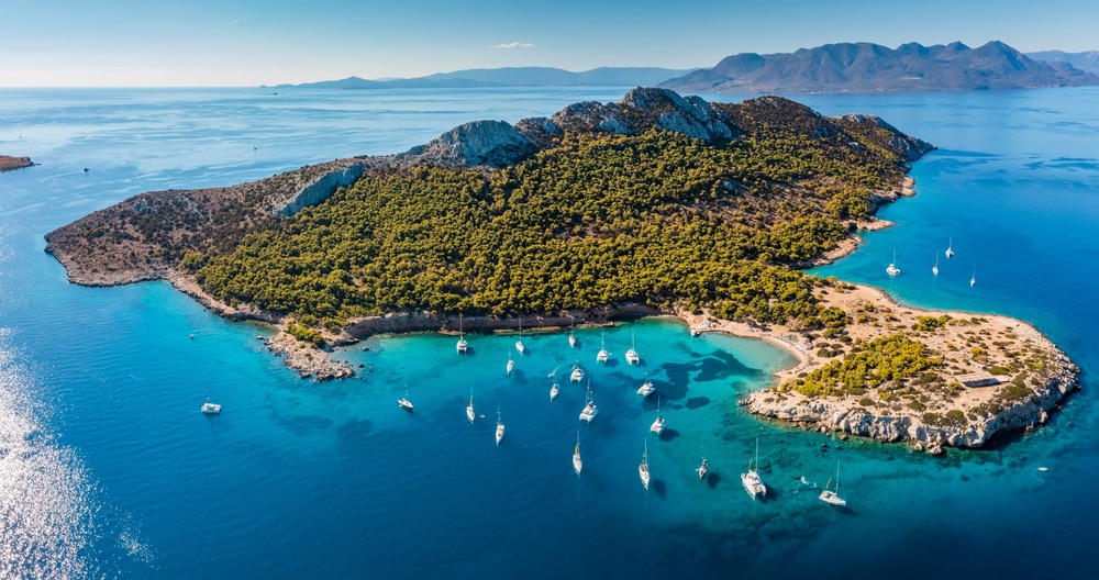 Yachts in turquoise water near the green island of Moni Eginas, Greece. Aerial view