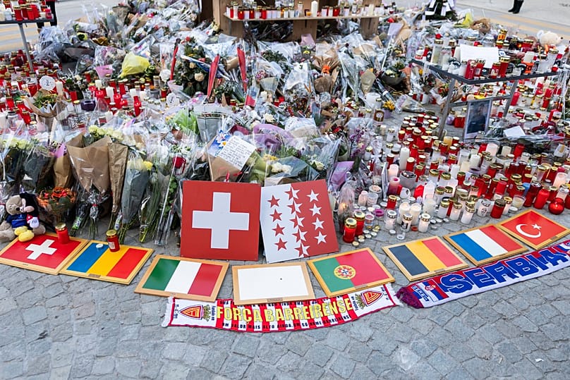 Plaques bearing international flags are placed alongside flowers and candles at the 