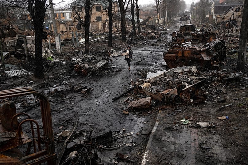 A woman navigates a debris-filled street where destroyed Russian military vehicles stand in Bucha on the outskirts of Kyiv, 3 April, 2022