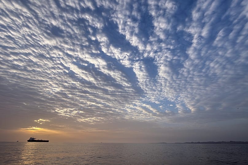 The sun rises behind a tanker anchored in the Strait of Hormuz off the coast of Qeshm Island, 18 April, 2026