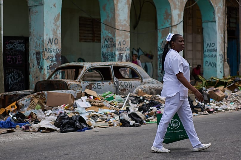 A nurse walks past trash and an abandoned classic American car on a street in Havana, Wednesday, April 22, 2026