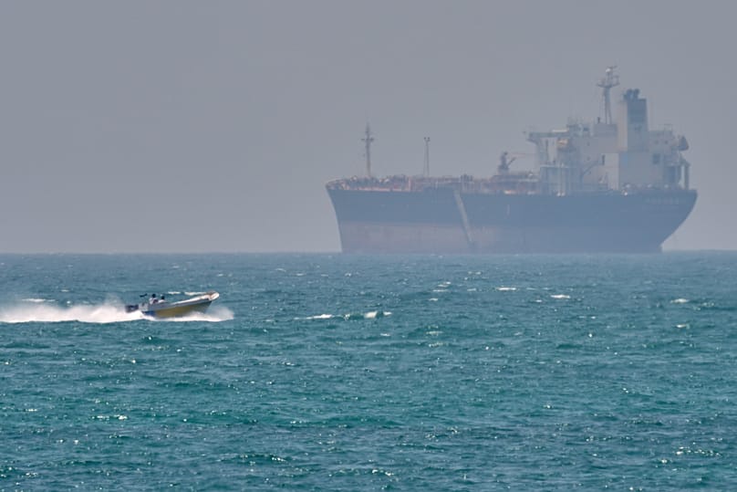 FILE: A boat sails past a tanker anchored on the Strait of Hormuz off the coast Qeshm island, Iran, 18 April 2026.