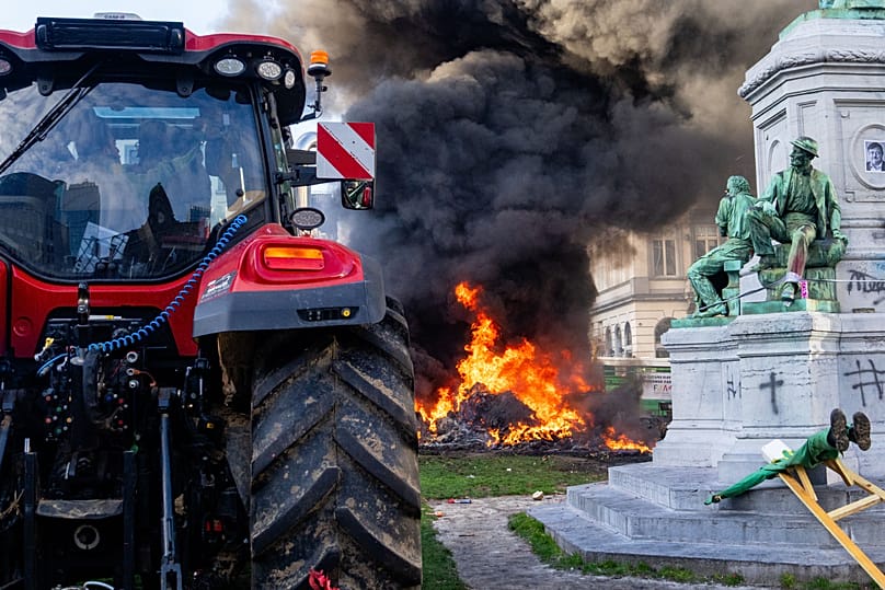 Protestors burn trash near a statue and tractor during a demonstration of European farmers near the European Parliament in Brussels, Thursday, Dec. 18, 2025.