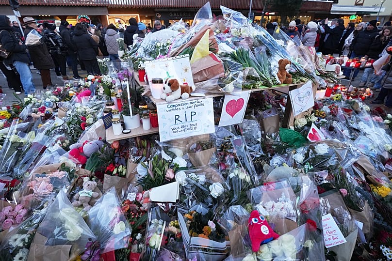 People stand around floral tributes and candles placed outside the sealed off Le Constellation bar in Crans-Montana, Swiss Alps, Switzerland, on Jan. 3, 2026.