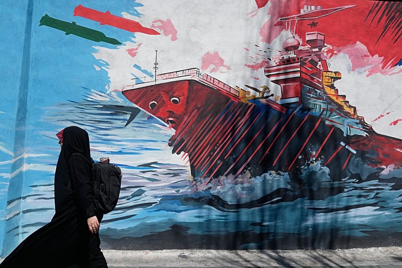 A woman walks past a mural depicting a US aircraft carrier under missile attack in downtown Tehran, 8 June, 2026