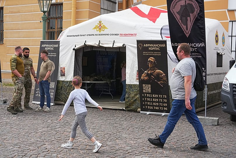 A child walks past a mobile recruiting centre in St Petersburg with a poster promoting contract military service in the African Corps, 12 June 2026