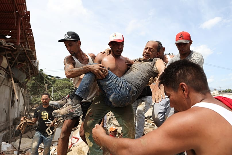 Neighbours carry a man rescued from the rubble of a collapsed building the day after earthquakes struck La Guaira, Venezuela, Thursday, June 25, 2026