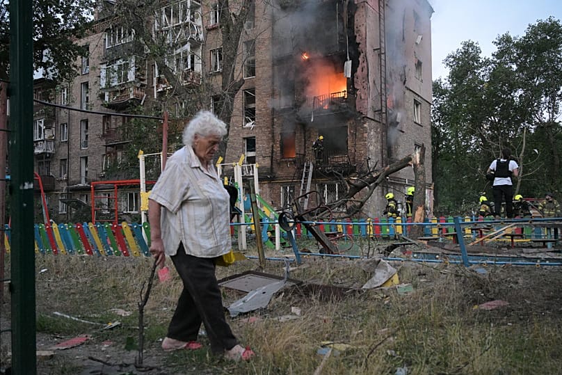 A woman walks past a burning apartment building after a Russian missile attack in Kyiv, 2 July, 2026