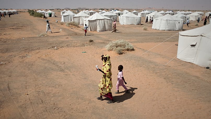 FILE - A woman and a child, displaced from North Darfur's capital walk in the newly established El-Afadh camp in Al Dabbah, Northern State, Sudan, Thursday, Nov. 13, 2025
