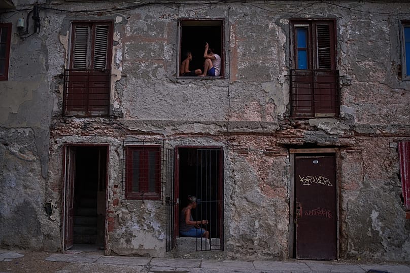 People catch the cool air from the street at their home's window during a blackout in Havana, 10 July, 2026