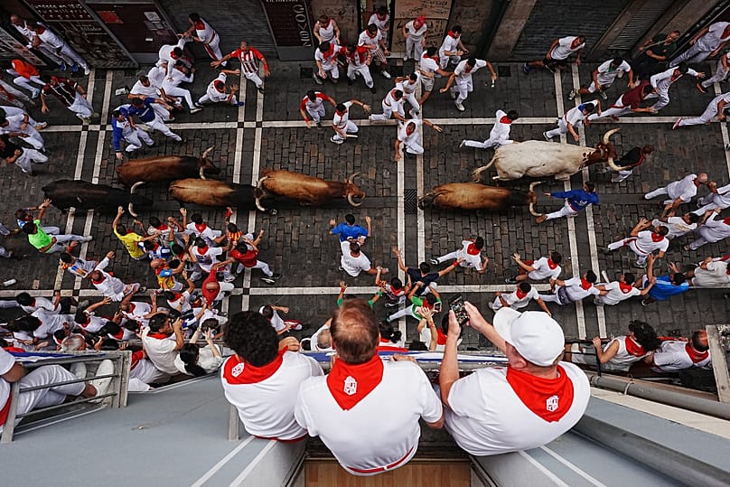 Revellers run alongside La Palmosilla's fighting bull during the sixth running of the bulls at the San Fermín festival, 12 July, 2026