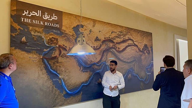 Visitors standing in front of a wall panel showing the route of the Silk Road at the Nas Tex 2026 exhibition at the Damascus fairgrounds