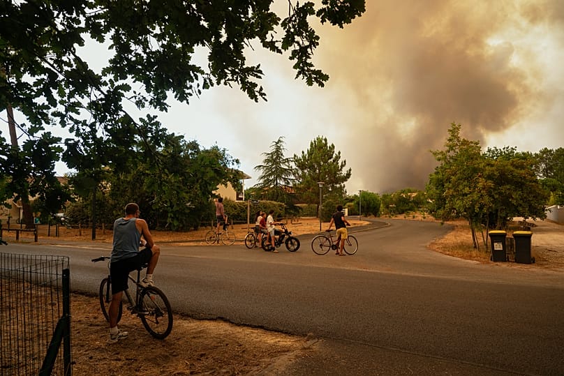 People watch massive plumes of smoke caused by wildfires in Le Porge, western France, Thursday, July 23, 2026.