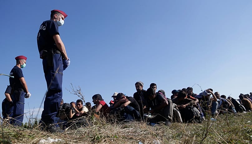 A group of migrants sits and waits to be escorted to a train after crossing a border from Croatia near the village of Zakany, Hungary, Wednesday, Sept. 23, 2015.
