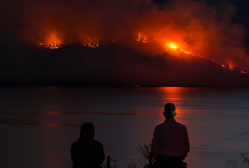 FILE - People in Lake Country, British Columbia, watch as the Quilpituk Creek wildfire burns on the mountainside across Okanagan Lake, near Fintry, Aug. 3, 2026. 