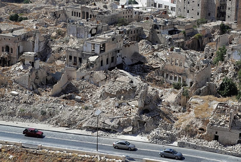 FILE: People drive their cars past destroyed buildings in the city of Aleppo, 16 August 2018