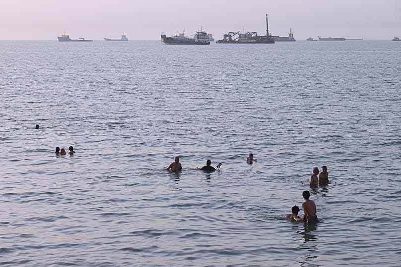 Residents swim as cargo and commercial vessels are anchored in the Strait of Hormuz off Bandar Abbas, 6 August, 2026