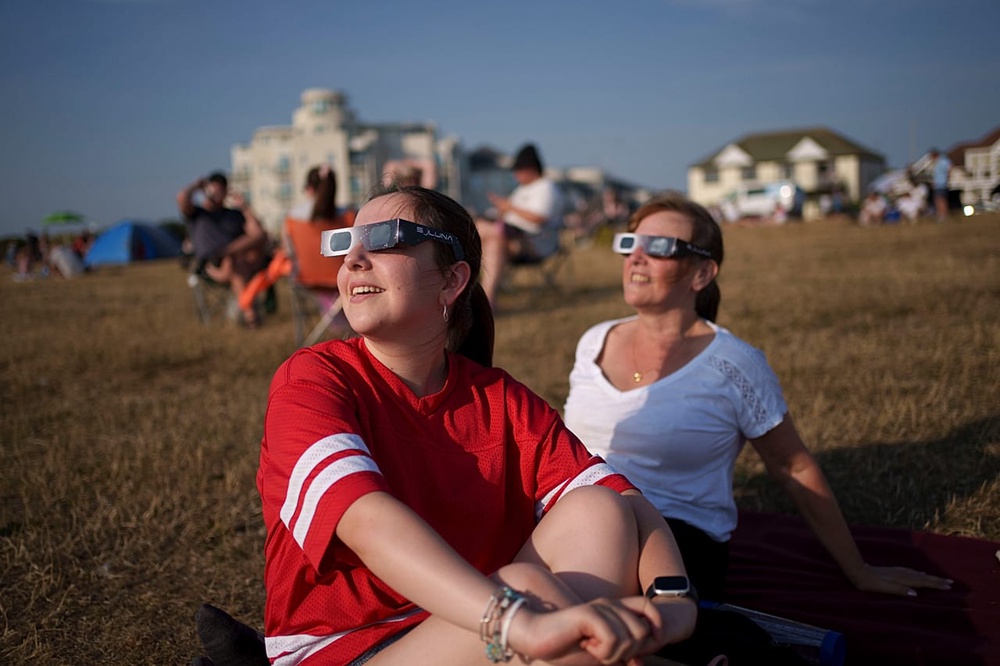 People observe a partial solar eclipse with special protective glasses at Crosby beach in Liverpool as the moon covers over 90 percent of the sun in Liverpool, England