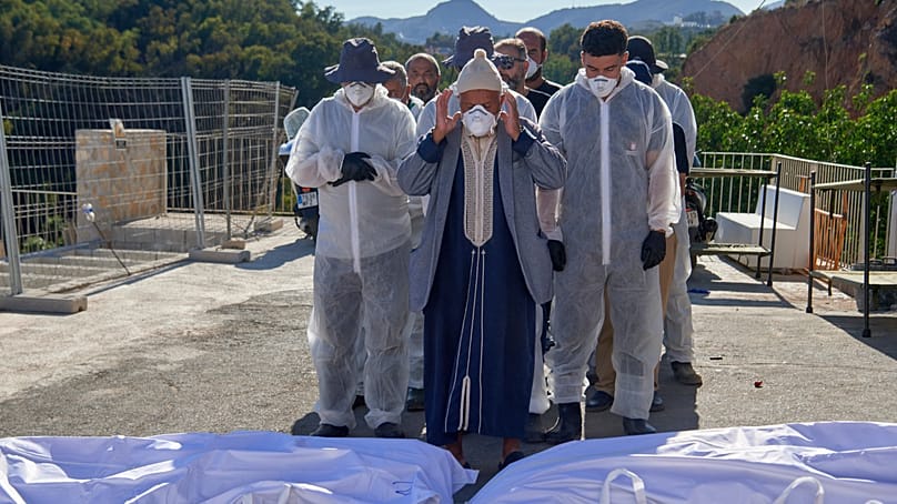A man, accompanied by funeral workers, prays over the bodies of migrants who died while trying to cross from Morocco to Ceuta, on 21 August 2026.