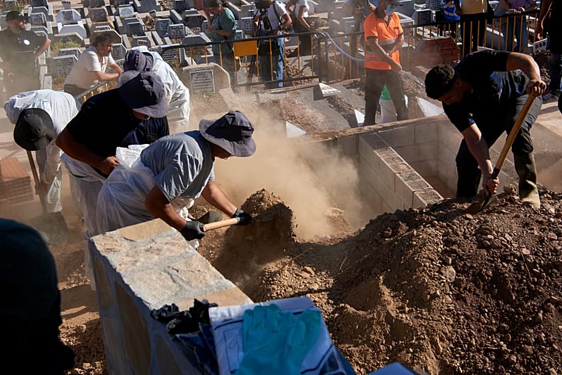 Funeral workers lower into a grave the body of a migrant who died while trying to cross from Morocco to Ceuta, on 21 August 2026.