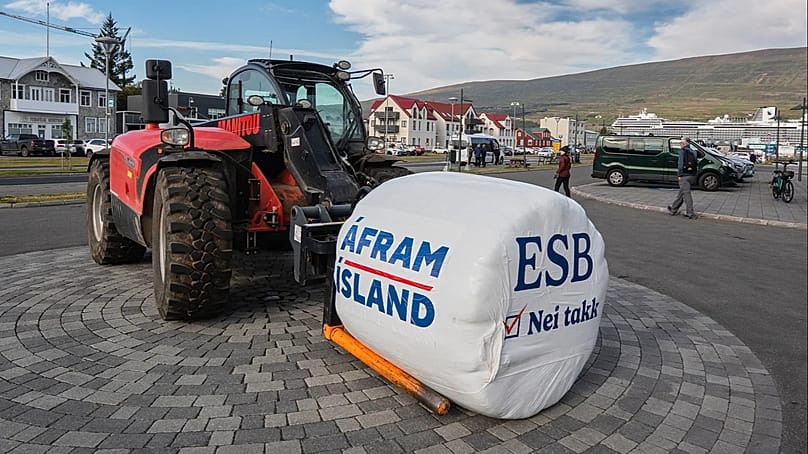 A loader carries a hay bale bearing the slogans 