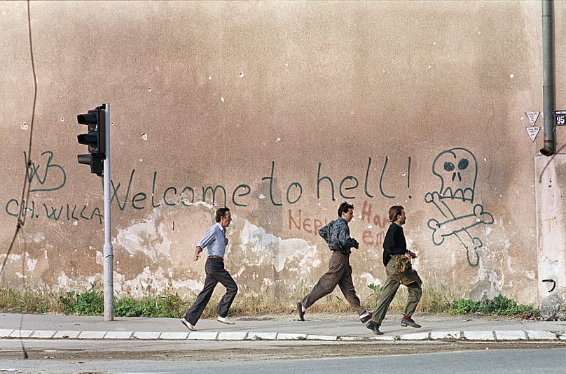 FILE: Three men run for cover past graffiti reading: 