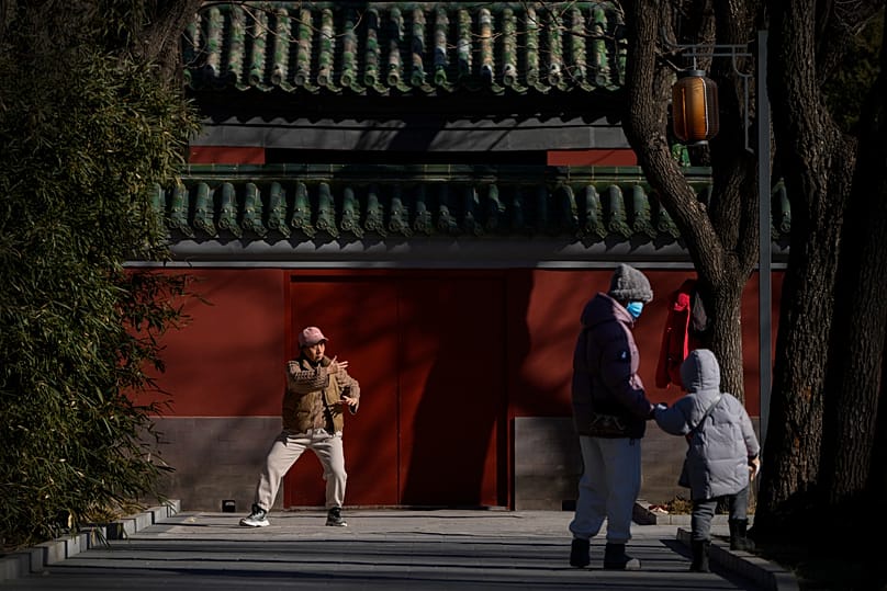 A woman and a child walk by as a woman practices tai chi at Ritan Park in Beijing.
