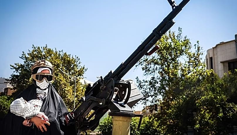 A woman holding a baby behind a machine gun