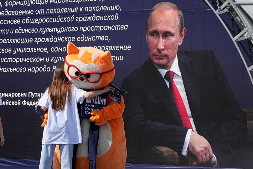 A woman hugs a performer in a cat costume next to a portrait of Russian President Vladimir Putin on Palace Square in St Petersburg, Russia, 21 May 2023.