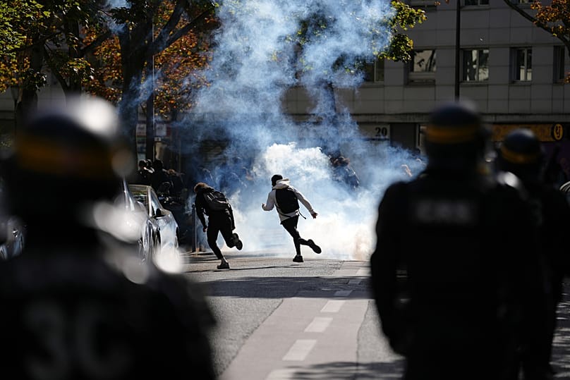 Students run through teargas as they face policemen during a protest against under-resourced schools, in Paris, Friday, Oct. 2, 202