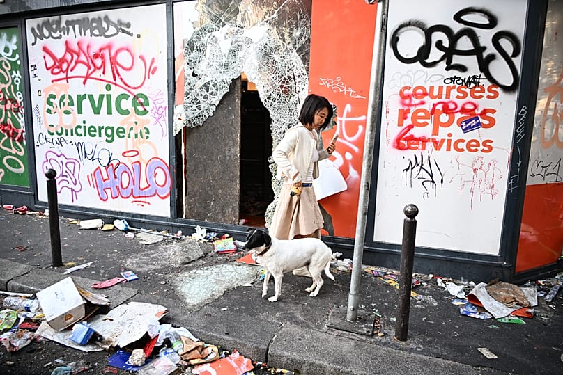 A woman walks her dog past a looted store the day after a demonstration against rising living costs in Paris, 18 October, 2026