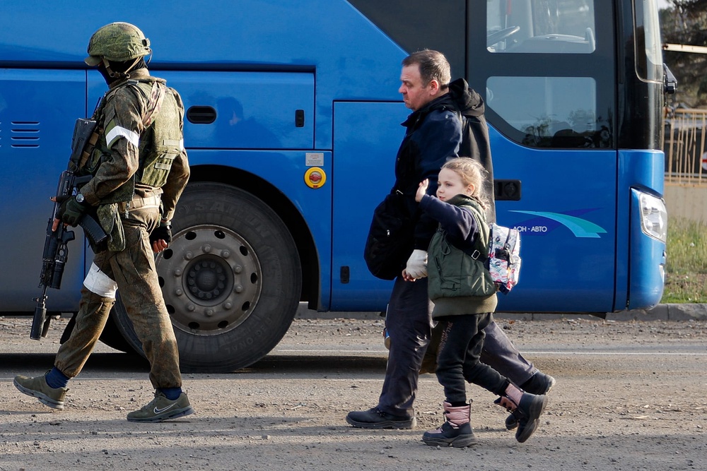 A man and a girl who left a shelter at Azovstal walk to a bus escorting by a serviceman of Russian Army in Mariupol, Ukraine, May 6, 2022. 