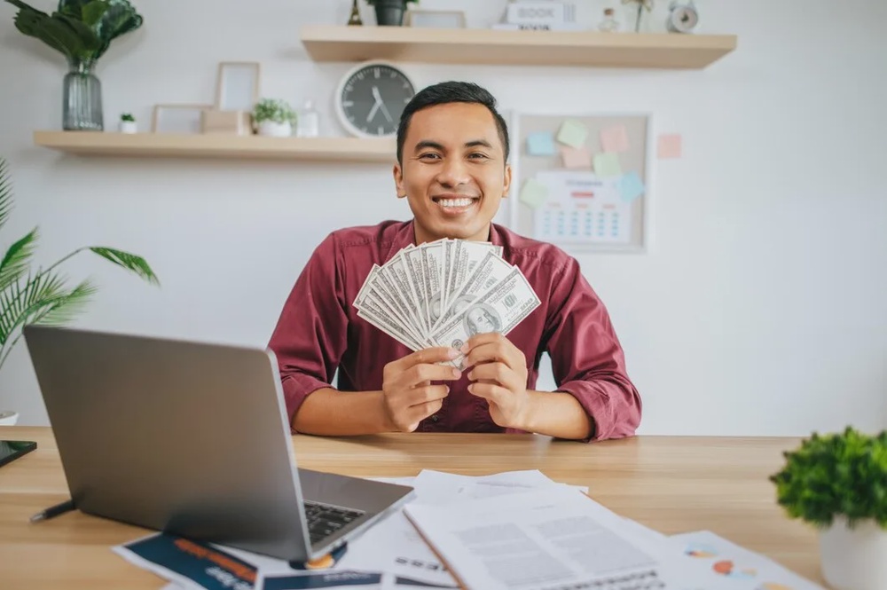 man working office holding money with laptop documents desk 1150 52076