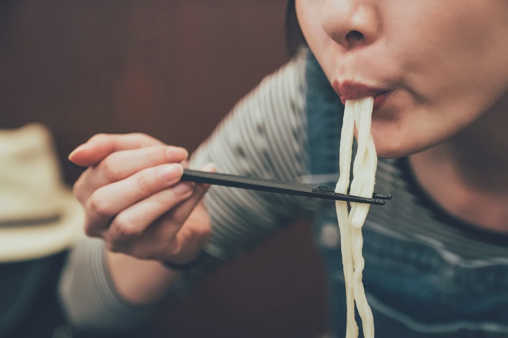 woman eating noodles using choptsicks