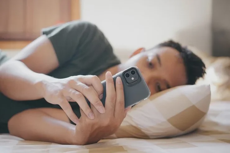 young man lying bed looking his smartphone with thoughtful expression relaxed cozy bedroom 885751 513