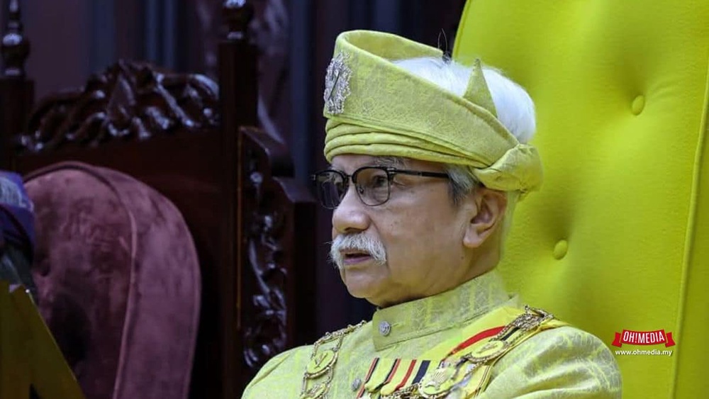Portrait of an elderly man in a yellow ceremonial outfit with a turban and glasses, seated on a yellow chair.