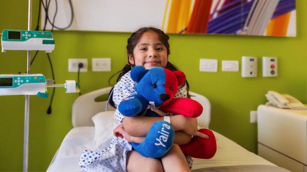 Seven-year-old Yaira hugs a teddy bear in a Mexico City hospital room while supported by Airbnb.org