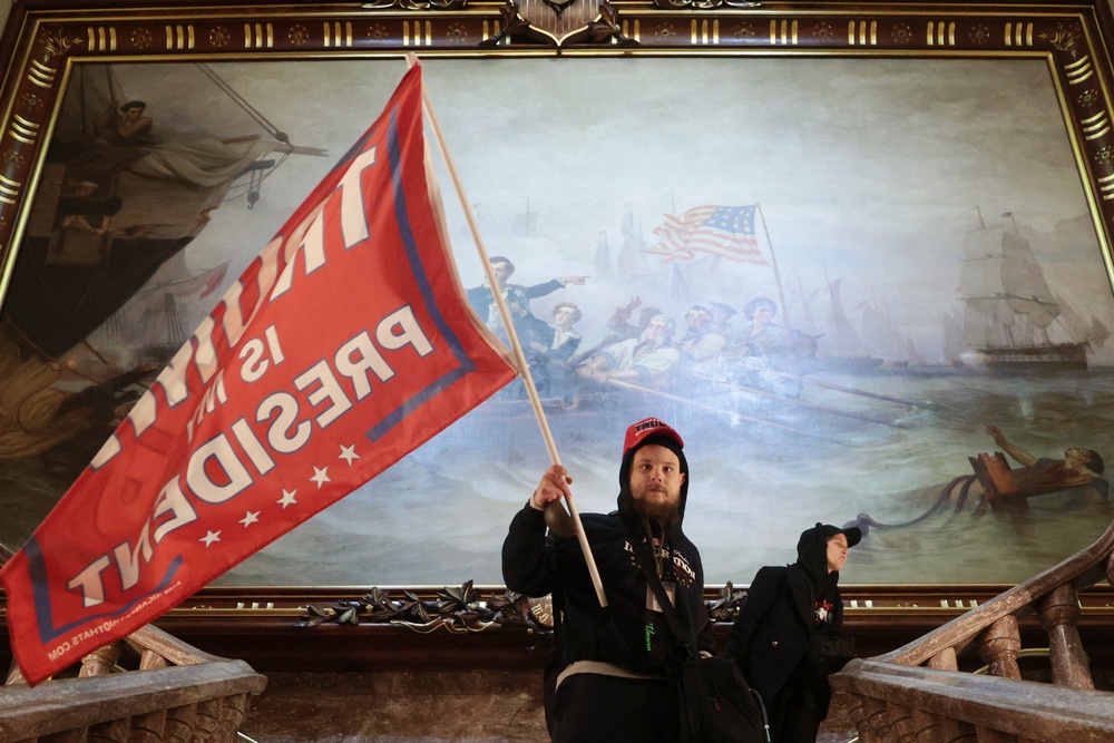 A protester waves a Trump flag inside the US Capitol building in front of a 19th century painting on 6 January, 2021. (Getty Images)