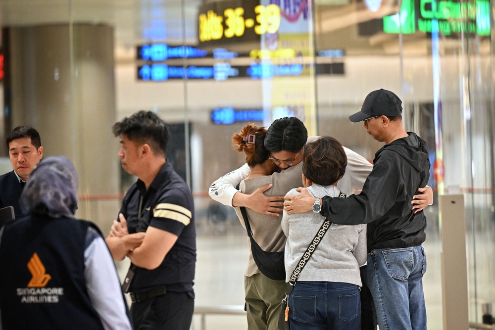 Passengers who experienced severe turbulence on a Singapore Airlines flight embrace after landing in Singapore (Reuters)