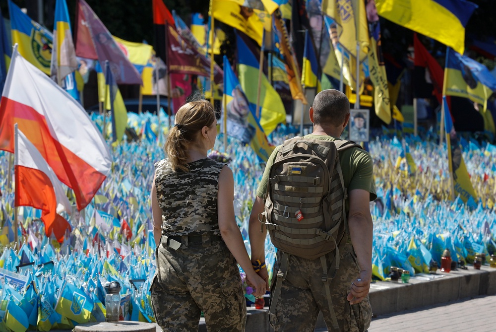 A  couple in uniform hold hands as they pass Ukrainian national flags set up commemorating fallen Ukrainian soldiers (EPA)