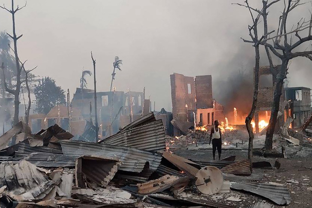 A man stands near a burning house following a suspected airstrike by Myanmar's military at Kyauk Ni Maw village in western Rakhine state on 9 January 2025 (AFP via Getty)