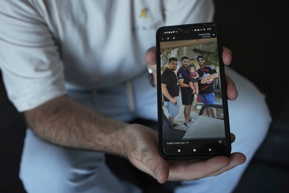 Liran Berman holds a picture on his mobile phone showing himself, right, and brothers, Ziv, left, and Gali, center, who were abducted by Hamas-led militants (Copyright 2025 The Associated Press. All rights reserved)