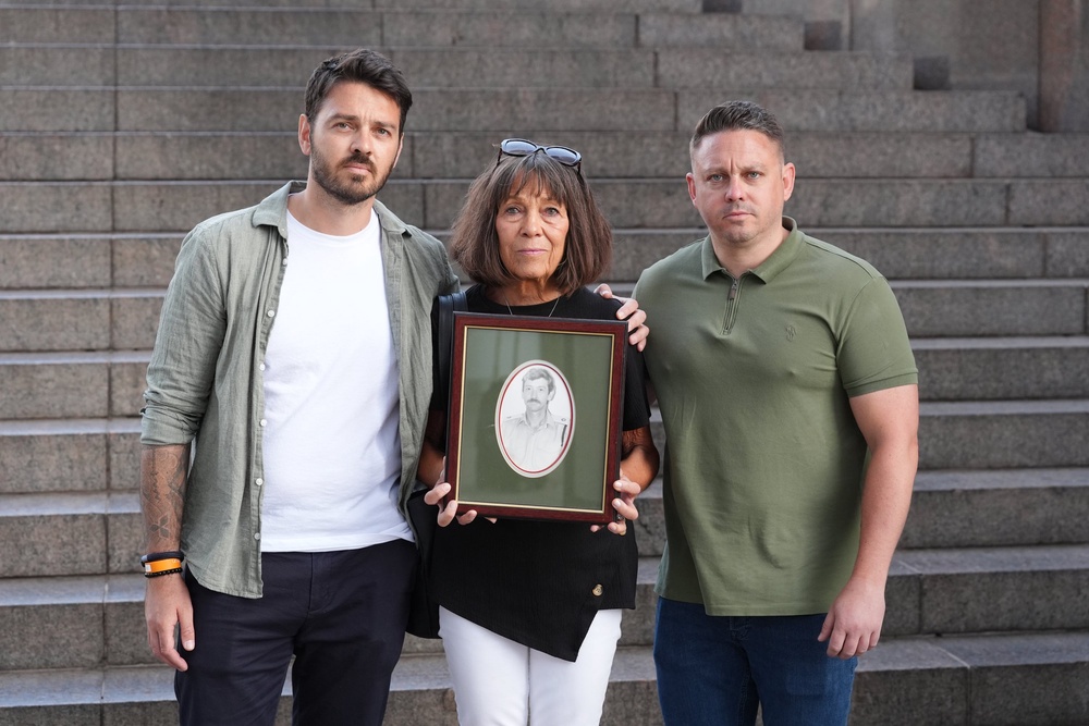Matt Tobias, right, with his brother Andy and mother Gaynor, who is holding a photo of the late Lieutenant Colonel John Tobias (PA Wire)