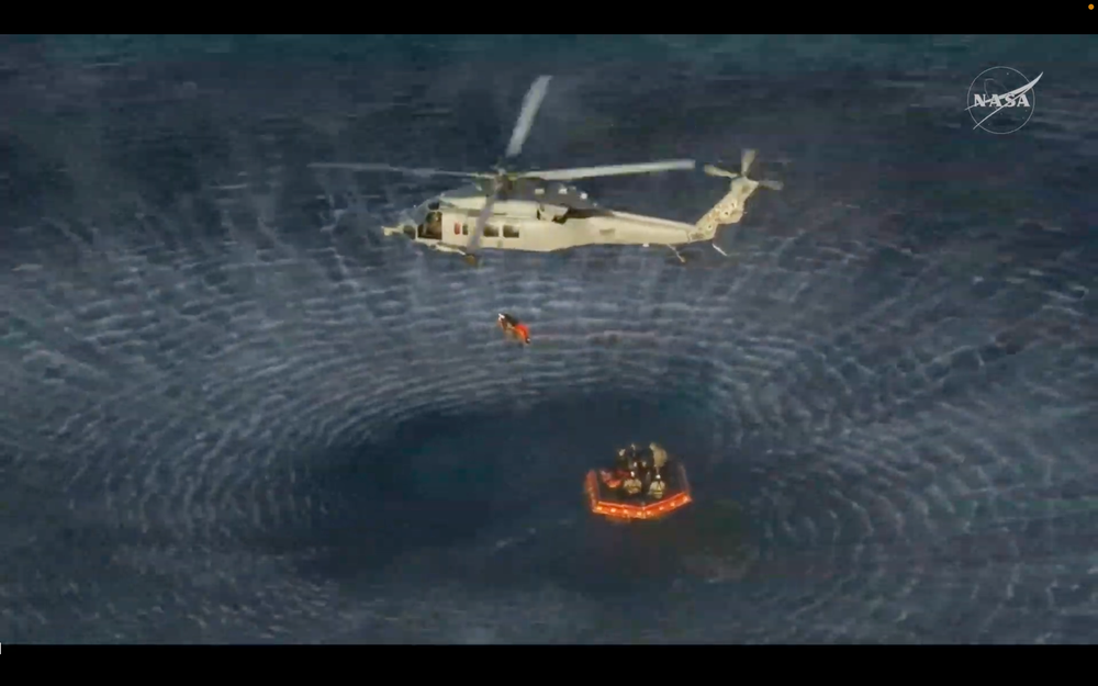 One of the Artemis II astronauts is hoisted beneath a helicopter to a U.S. Navy recovery ship (NASA via YouTube)