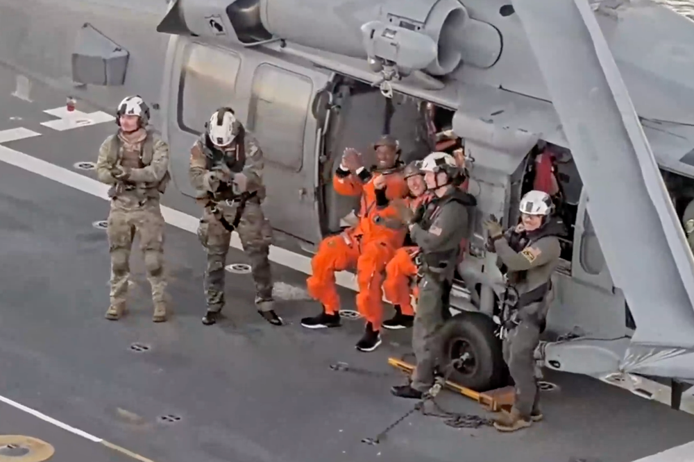Artemis II astronauts Victor Glover and Christina Koch wave and salute to the camera after safely landing on the USS John P. Murtha following their return from lunar space (NASA via YouTube)