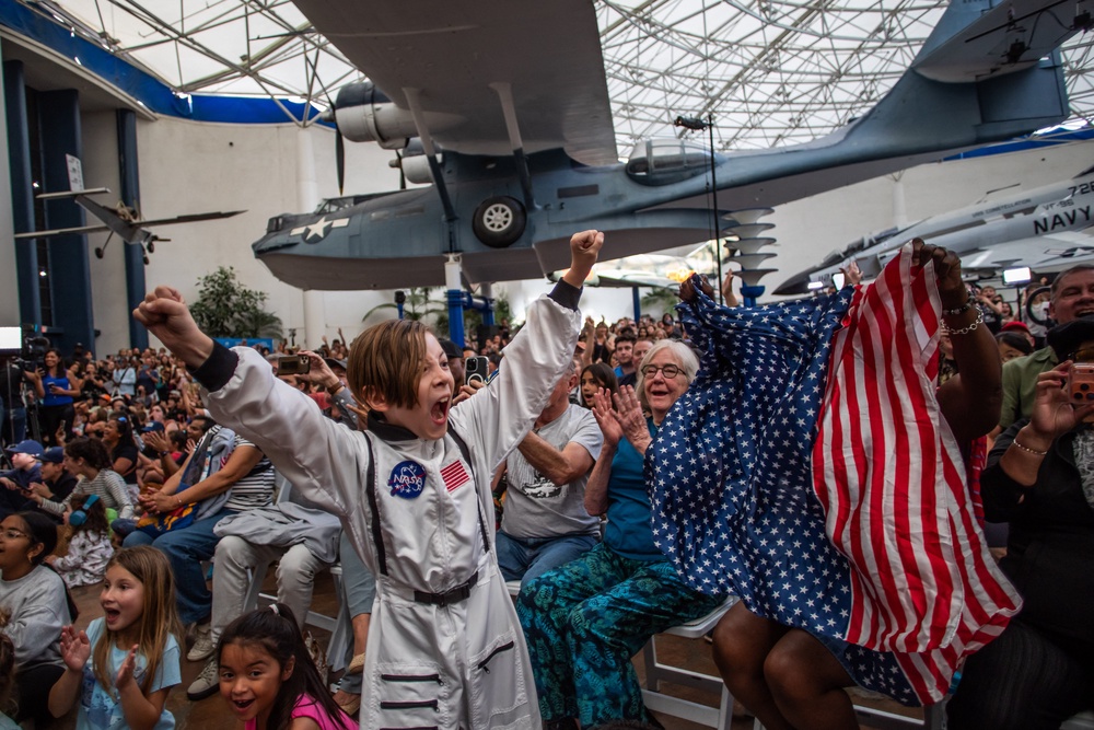 A young boy wearing an astronaut costume cheers next to a woman waving a flag as they watch a live broadcast of the return of the Artemis II crew members to Earth at the San Diego Air and Space Museum during a watch party for the crew's splash down in the Pacific Ocean, in San Diego, California, on April 10, 2026. (Apu GOMES / AFP via Getty Images)